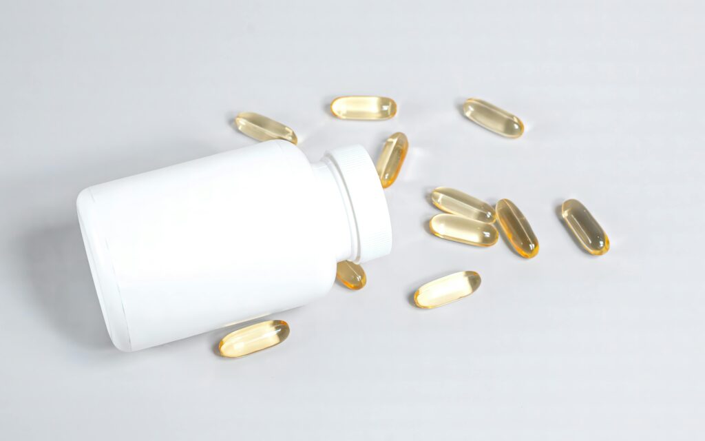 Healthy fish oil capsules spilled from a white bottle on a smooth white surface.